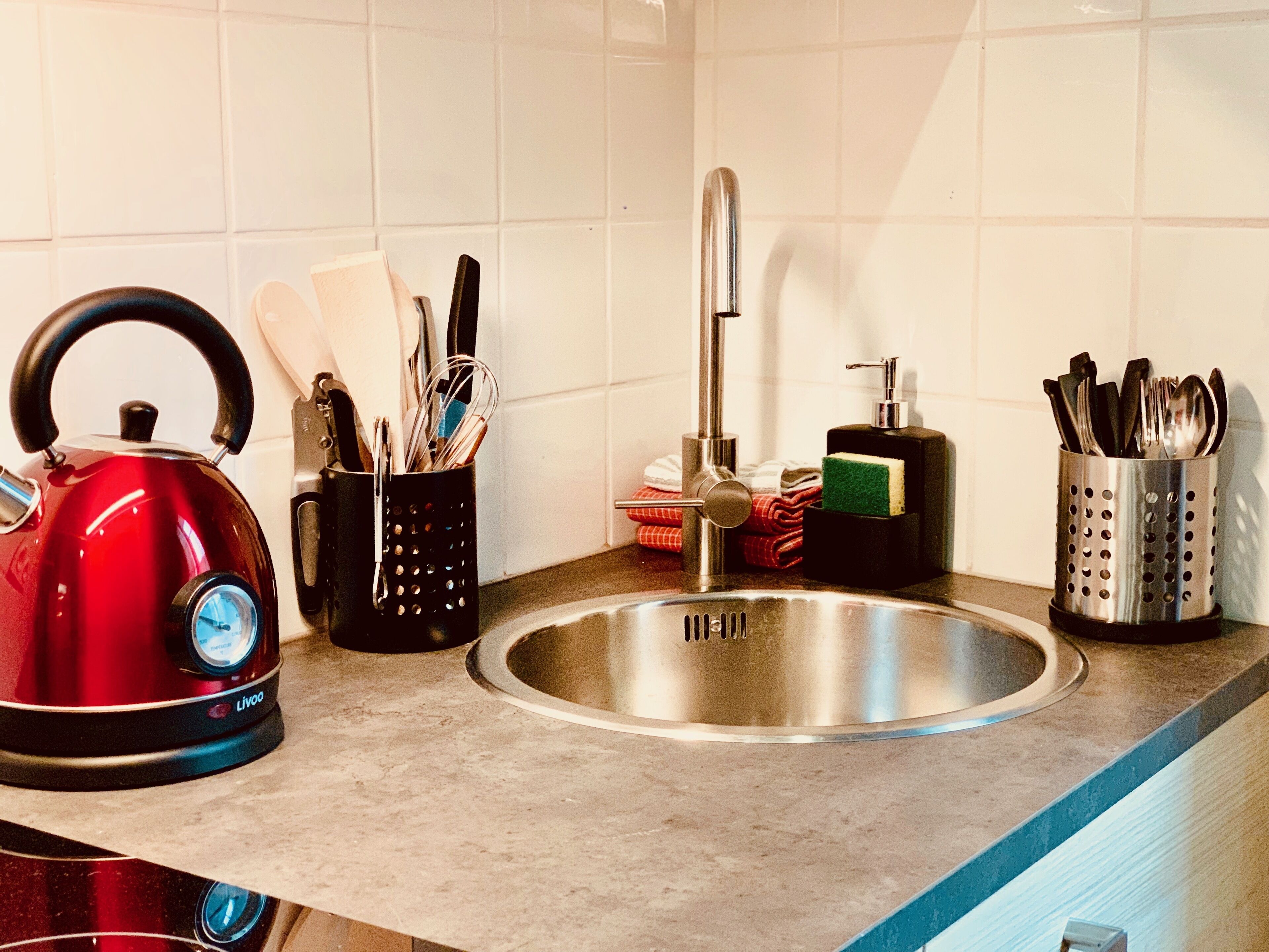 Una cocina con un hervidor rojo, un lavamanos y utensilios en organizadores.