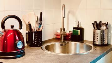 Una cocina con un hervidor rojo, un lavamanos y utensilios en organizadores.