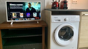 Een keuken met een wasmachine en een televisie waarop Netflix draait.