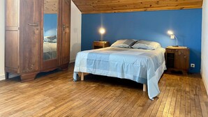 Ein Schlafzimmer mit Holzboden, einem Bett mit blauer Bettdecke, zwei Nachttischen mit Lampen und einem Holzschrank.