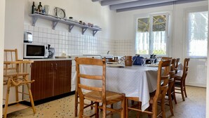 Ein Essbereich mit einem Tisch für sechs Personen, Holzkästen und einer Küchenzeile inklusive Mikrowelle, Toaster und Regalen mit Küchenutensilien.