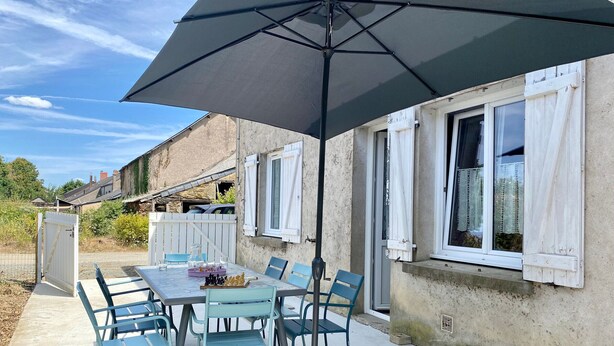 Eine Terrasse im Freien mit Tisch und Stühlen, einem großen Sonnenschirm und Blick auf ein Wohngebäude.