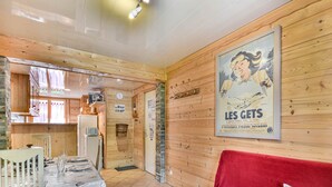 A cozy room with a wooden interior, a dining table set with plates and glasses, a red sofa with decorative pillows, and a poster on the wall. - Newly Renovated 2BR Apartment Near Mont Chéry Cable Car - Les Gets, Sleeps 5 (Les Gets)