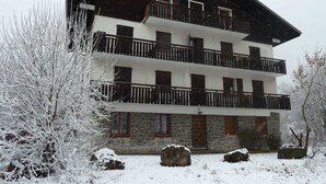 A multi-story building with balconies, stone walls, and snow-covered surroundings. - Newly Renovated 2BR Apartment Near Mont Chéry Cable Car - Les Gets, Sleeps 5 (Les Gets)