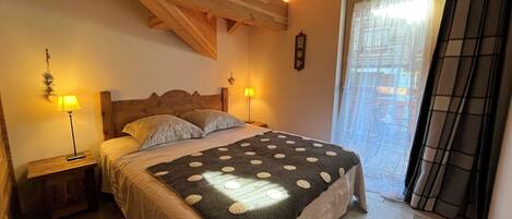Ein Schlafzimmer mit Holzboden, einem Bett mit gepunkteter Decke, zwei Nachttischlampen und Blick durch eine Tür mit Vorhängen.