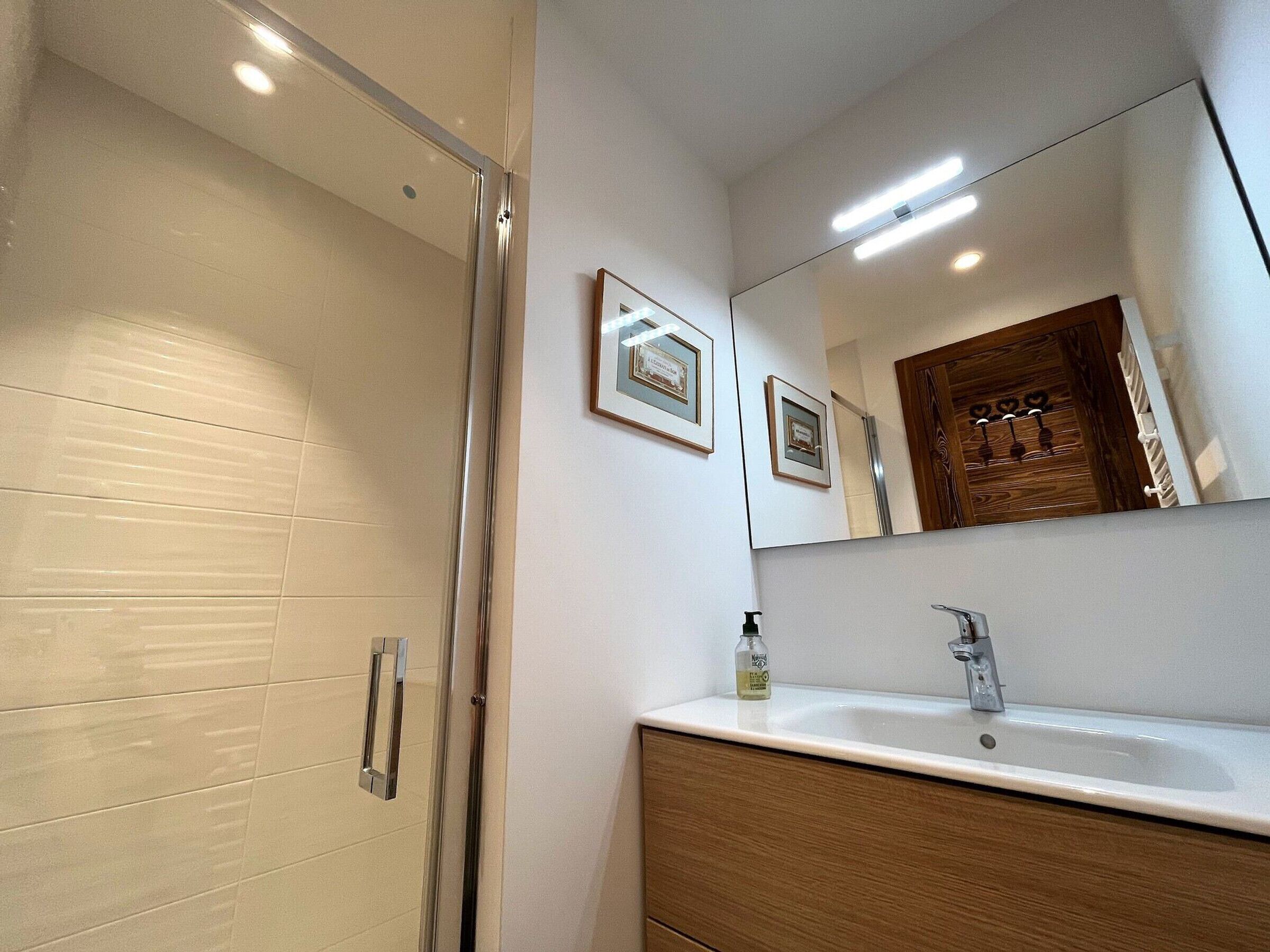 Um banheiro moderno com box de vidro, pia branca e toucador de madeira.