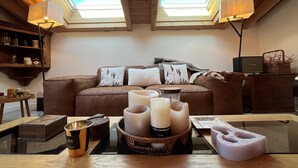 Ein gemütliches Wohnzimmer mit einem braunen Ledersofa, zwei Oberlichtern und einem Glastisch mit Kerzen und einer Ablagefläche.