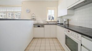 Una cocina compacta con armarios blancos, microondas, lavavajillas y ventana con vistas a edificios.