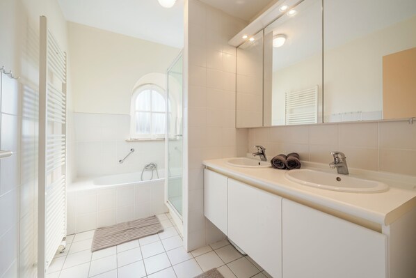 Une salle de bain moderne dotée d’une douche à l’italienne, d’un meuble-lavabo à deux vasques et d’un grand miroir.