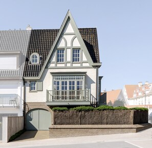Une maison à deux étages, avec un toit à pignon, un porche à l’avant et un mur en briques.