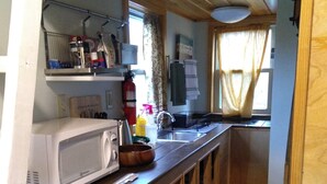 A compact kitchen with a microwave, sink, and wooden cabinets. - Tiny House Retreat Cabin (Freeville)