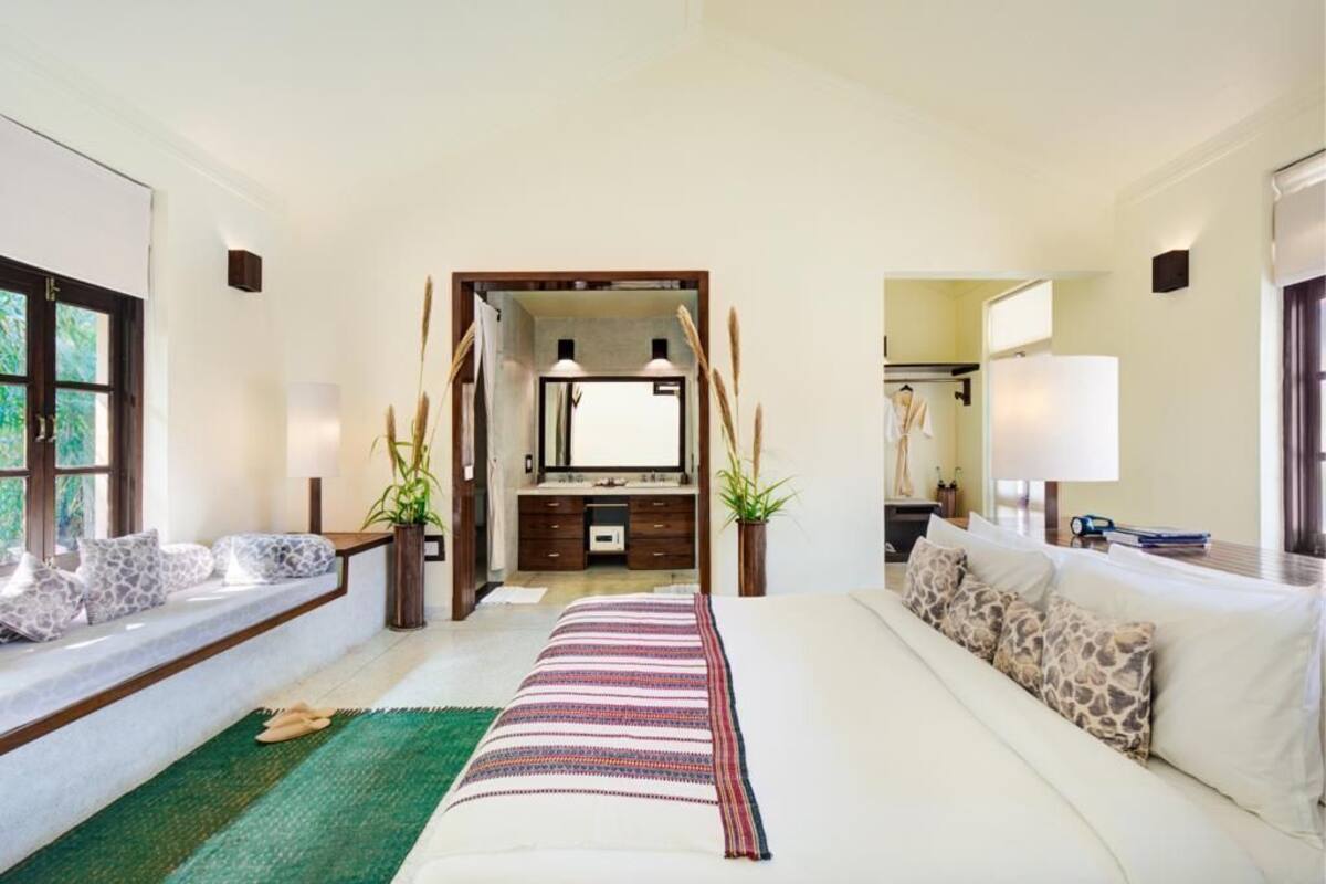 A hotel room with a bed, a sofa, a window with a view, a mirror, and a bathroom visible through an open door.