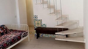A room with a white bed, a small table, and a unique spiral staircase. - Positano Little House. Sea view. White Dome.Terrace&WinePergola.15minToTheBeach (Positano)