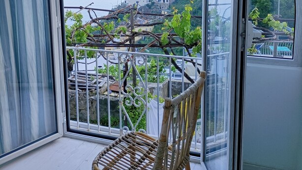A balcony with a view of a coastal town, a chair, and a metal railing. - Positano Little House. Sea view. White Dome.Terrace&WinePergola.15minToTheBeach (Positano)