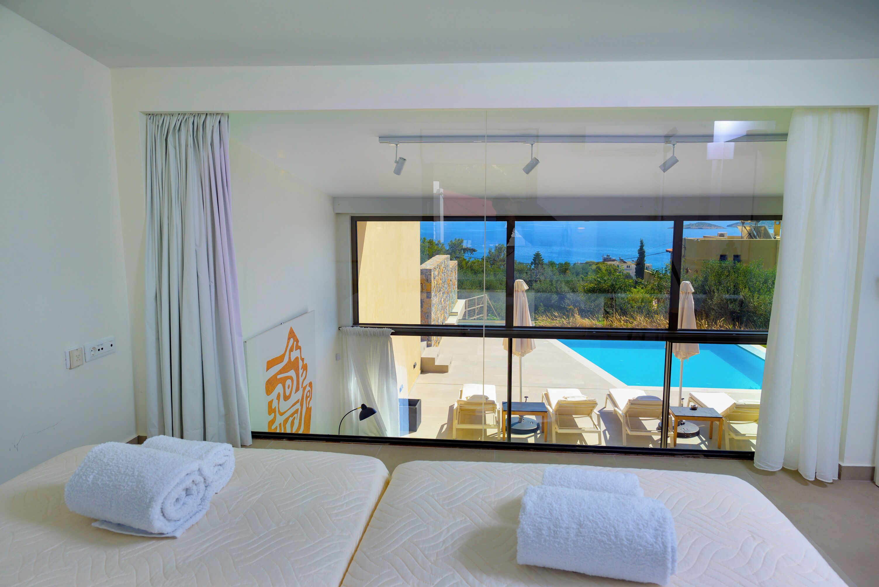 A hotel room with two beds, a large window with a view of a swimming pool and buildings, and a balcony with chairs and tables.