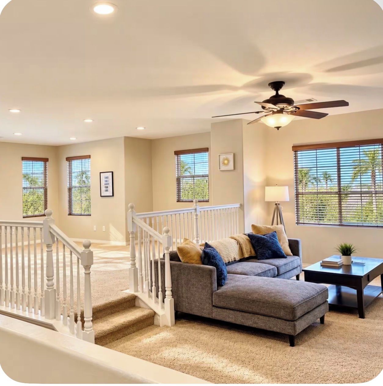 A spacious living area with a staircase, a ceiling fan, and large windows.