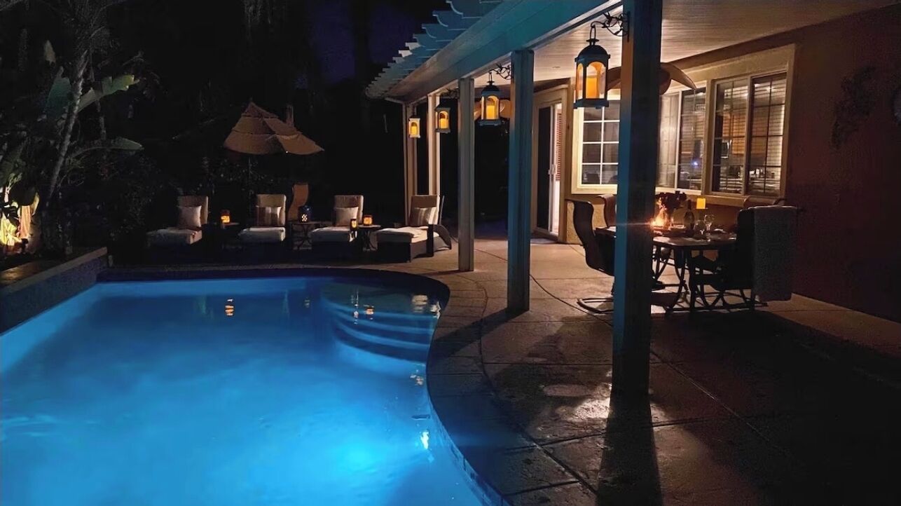 A swimming pool with lounge chairs and tables, surrounded by a covered patio area with hanging lanterns.
