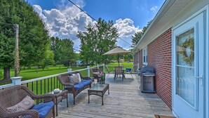 A wooden deck with wicker furniture, a grill, and a view of a green lawn and trees. - Charming Retreat on 5 Acres w/ Deck & Grill! (Browns Summit)