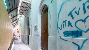 Une ruelle étroite, avec un bâtiment sur la droite, caractérisé par une porte en bois et un mur couvert de graffitis.
