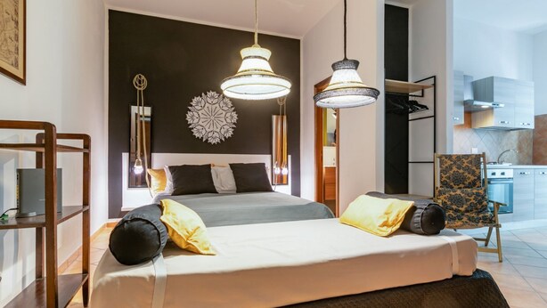 Une chambre moderne avec un grand lit, deux lampes suspendues, un élément décoratif mural et une vue sur la cuisine.