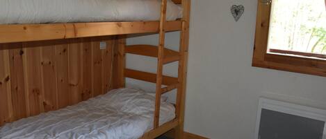 Ein Schlafraum mit Etagenbetten, einem Fenster, Holzwänden und einer Heizung.