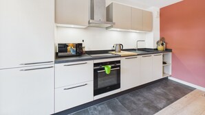 A modern kitchen with white cabinets, a stainless steel range hood, a black countertop, and a built-in oven.