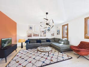 Ein modernes Wohnzimmer mit einem Ecksofa, einem roten Sessel, einem Couchtisch und einem Fernseher auf einem Schrank.