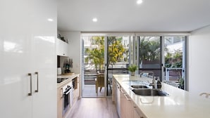 A modern kitchen with a large island, built-in appliances, and a view of the city through large windows. - Riverside luxury apartment across two levels at Waterline. (Forster)