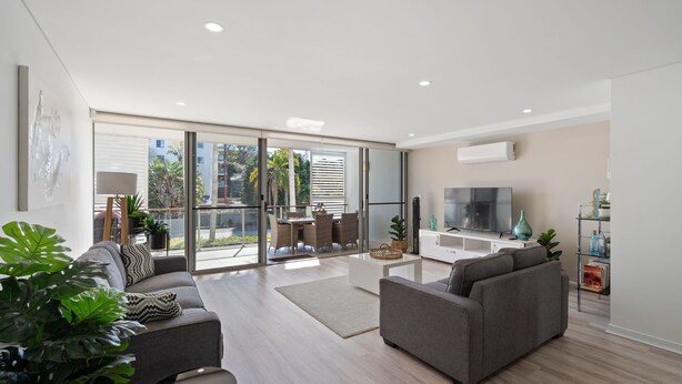 A modern living room with a sofa, a coffee table, and a TV. There is a balcony with a table and chairs. - Riverside luxury apartment across two levels at Waterline. (Forster)