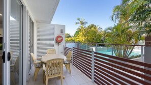 Un balcon avec une table et des chaises, un enrouleur de tuyau d’incendie et une piscine en arrière-plan.