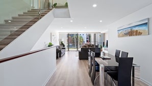 A modern interior with a staircase, a dining area, and a living space with a large window. - Riverside luxury apartment across two levels at Waterline. (Forster)