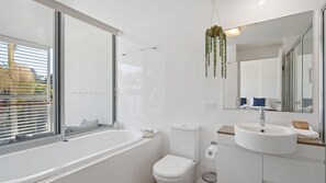 Une salle de bain moderne dotée d’une grande fenêtre, d’une baignoire, de toilettes et d’un lavabo.