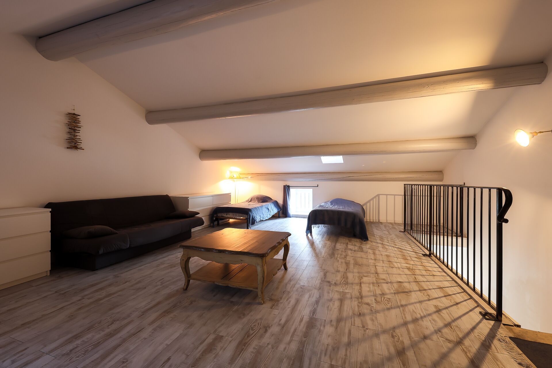 Amplio dormitorio tipo loft con techo alto, vigas de madera a la vista, un ventanal grande y un balcón con barandilla metálica.