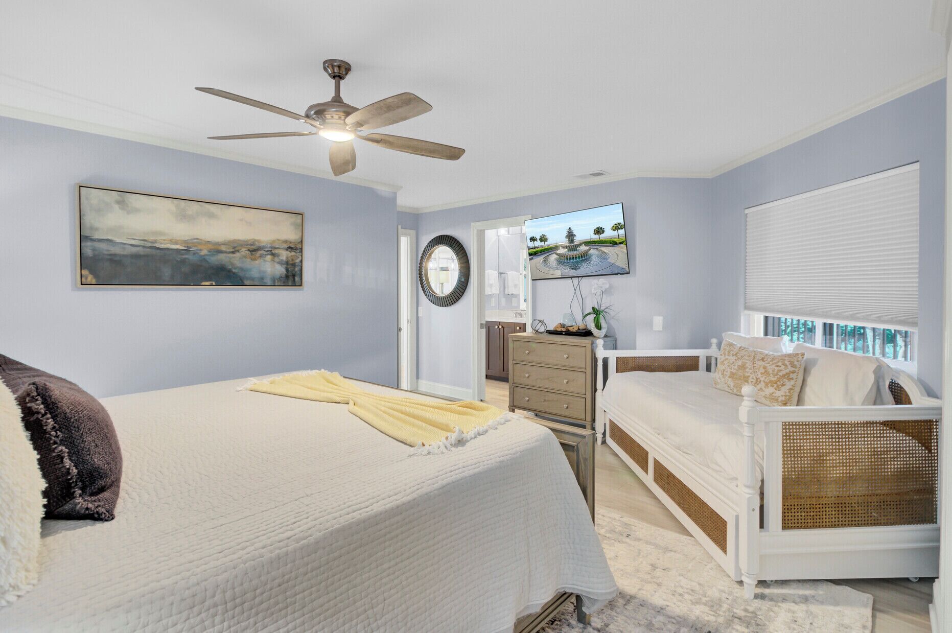 Un dormitorio con cama, cómoda, silla, ventilador de techo y televisor en la pared.