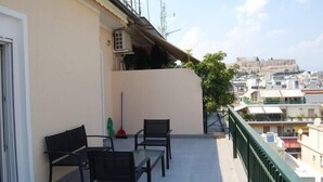 A balcony with a table and chairs, a mop, and a window with an air conditioning unit. - GTD33702 - Feel the Acropolis Apt (Athens)