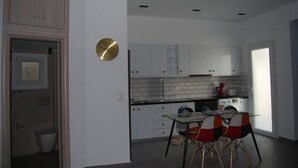 A modern kitchen with white cabinets, a black countertop, and a dining area with a table and chairs. - GTD33702 - Feel the Acropolis Apt (Athens)