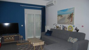 A living room with a grey sofa, a wooden coffee table, a TV, and a painting of a beach scene. - GTD33702 - Feel the Acropolis Apt (Athens)