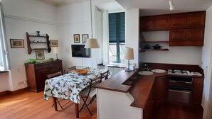 Cozinha compacta com armários de madeira, uma mesa de jantar com toalha de mesa florida e fogão embutido.