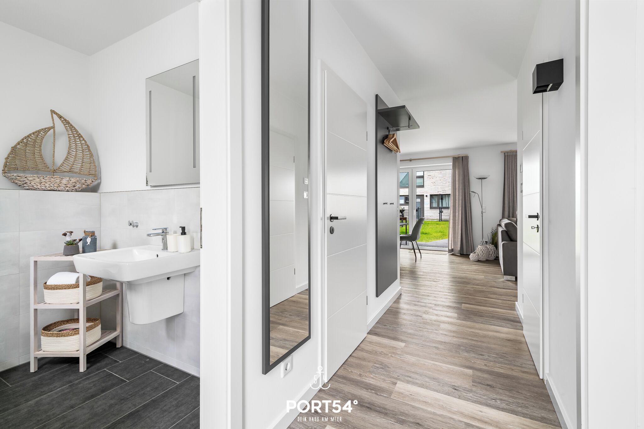 A modern bathroom with a white sink, mirror, and wooden flooring.