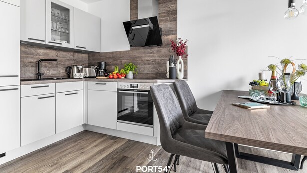 Una cucina moderna con mobili bianchi, forno integrato e zona pranzo con tavolo e sedie in legno.