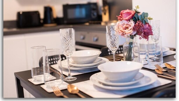 Ein Esstisch, gedeckt mit klarem Glas, weißen Tellern und einer Blumenarrangements.