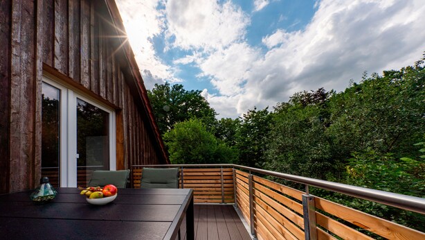 Eine Holzterrasse mit Tisch und Stühlen, einer Obstschale und Blick auf Bäume und Himmel.