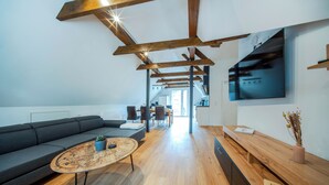 Ein modernes Wohnzimmer mit Holzbalkendecke, einem großen Fernseher und einem Essbereich.