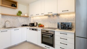 Cozinha moderna com armários brancos, geladeira de aço inoxidável, forno embutido e cafeteira.