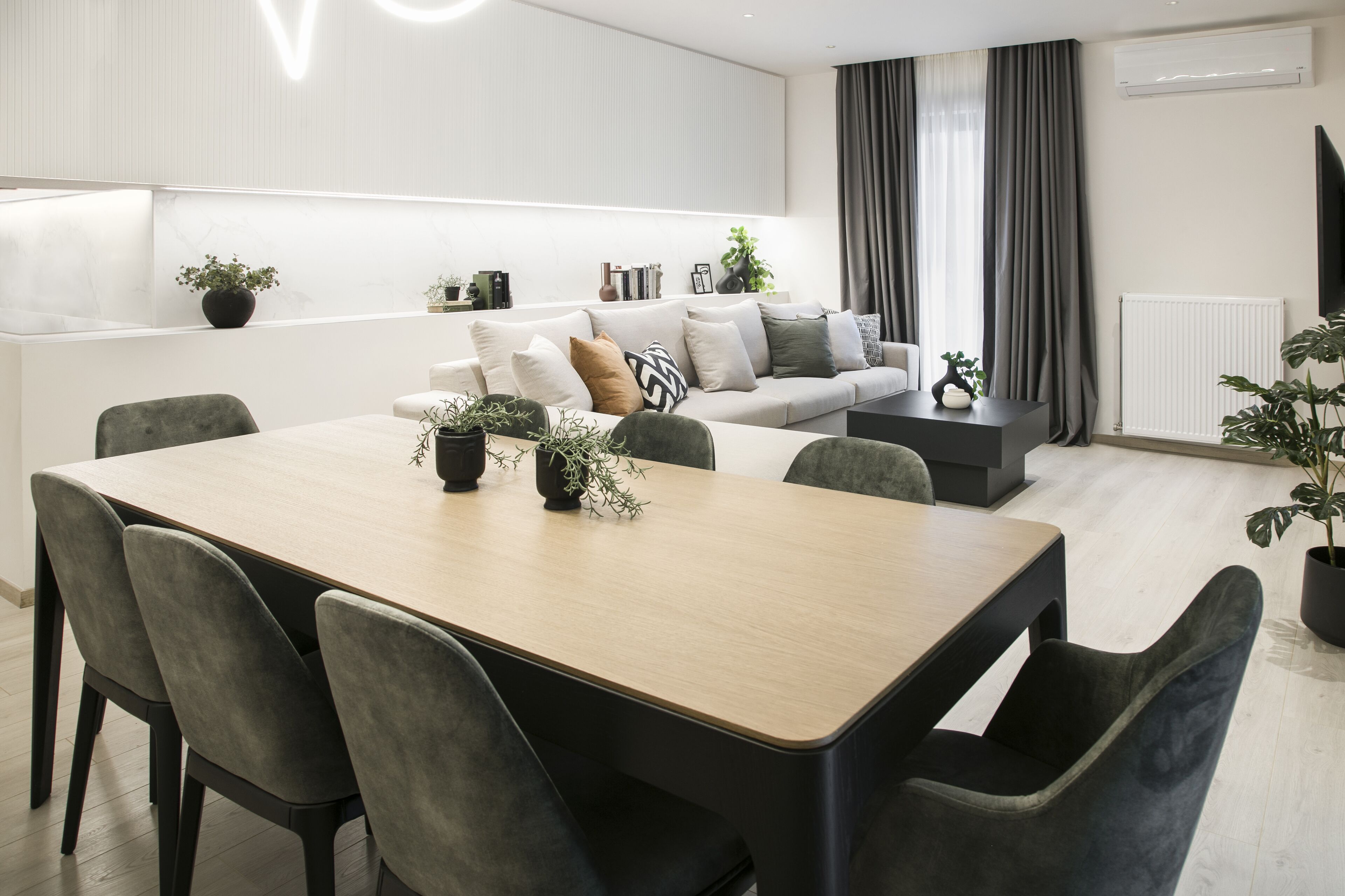 Un salon moderne avec un coin repas, comprenant un ensemble de canapés, une table basse et plusieurs plantes en pot.