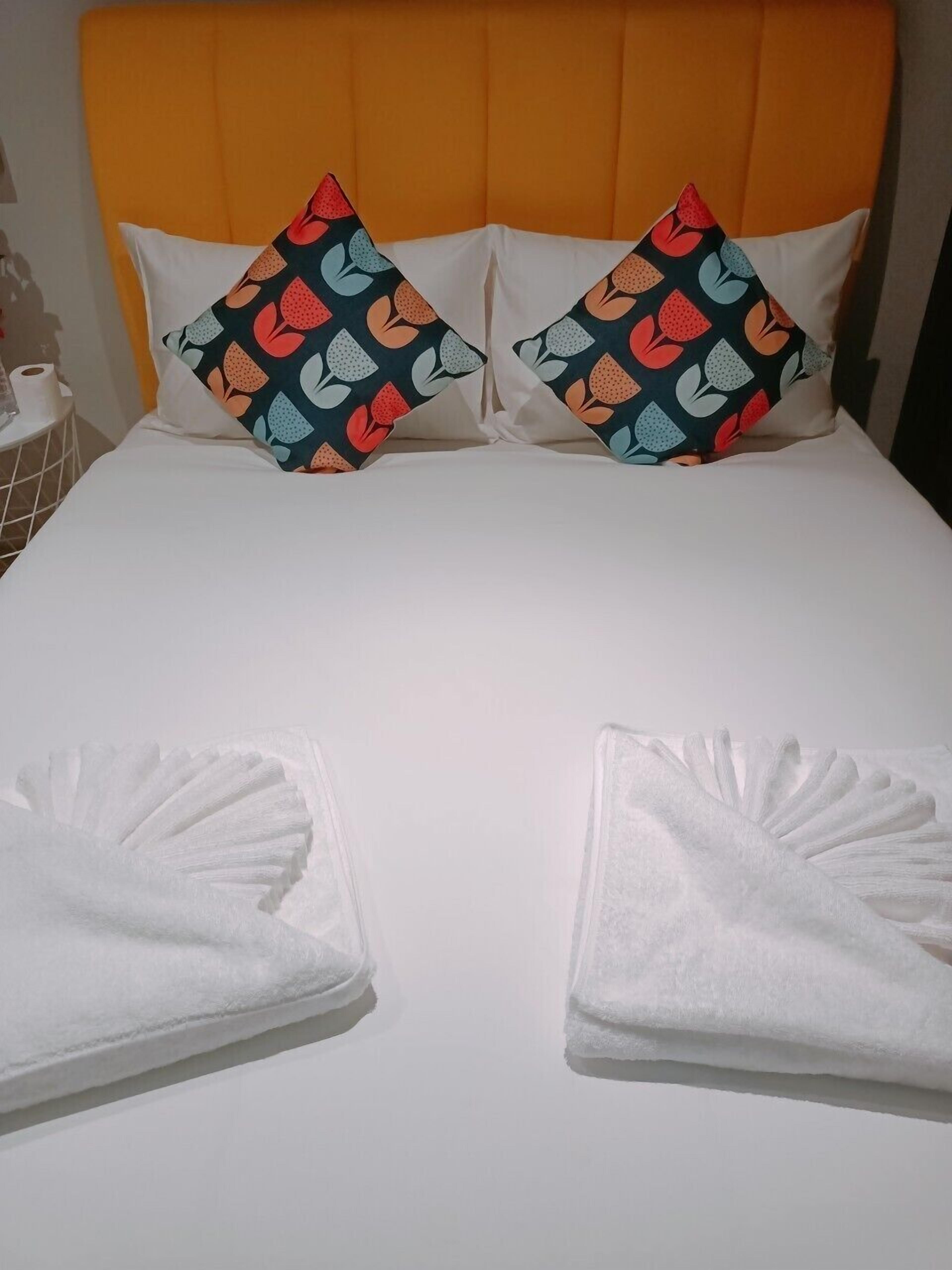 A hotel room with a bed, two pillows with a fruit pattern, and two folded white towels.