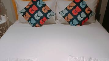 A hotel room with a bed, two pillows with a fruit pattern, and two folded white towels.