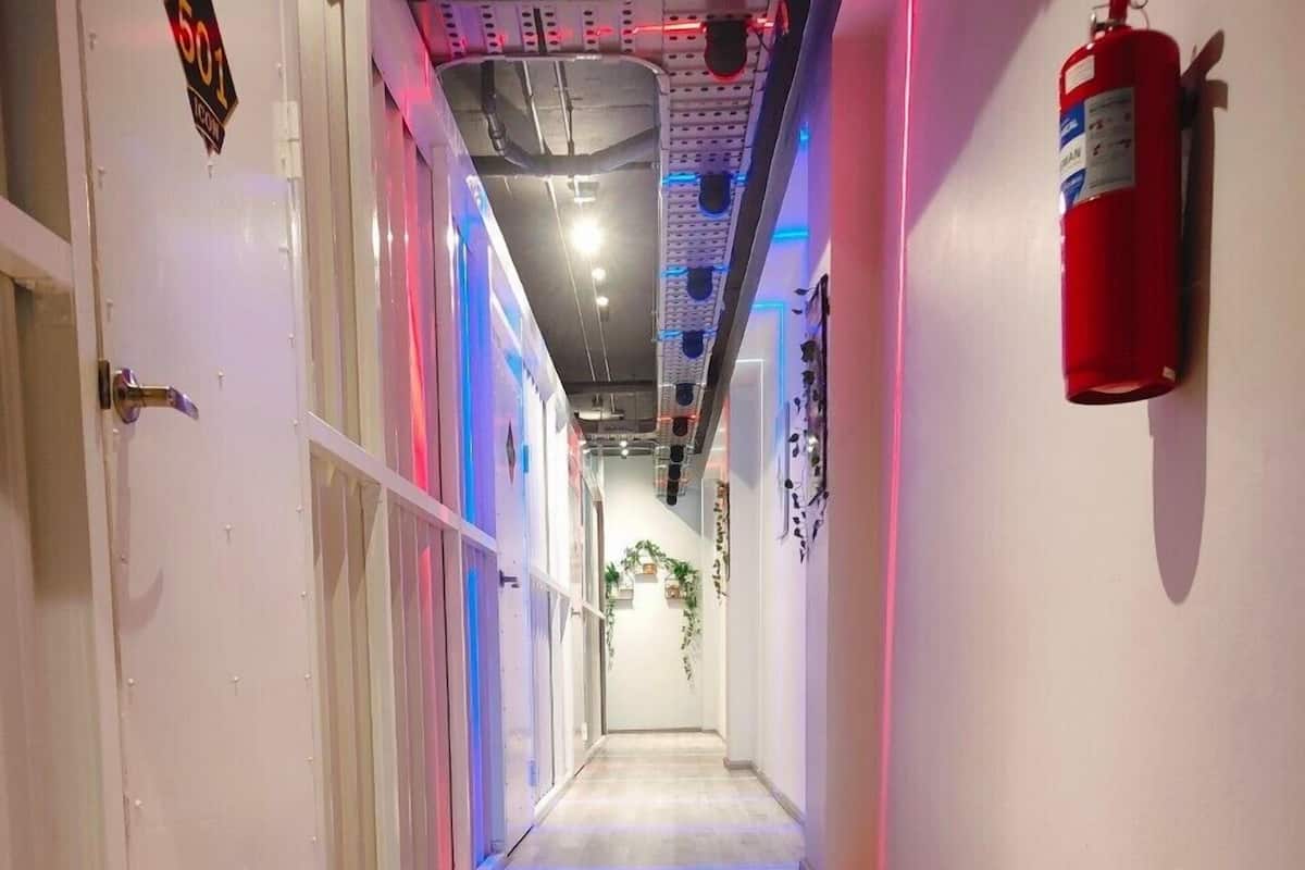 A hallway with a wooden floor, a fire extinguisher on the right, and a door with a sign on the left.