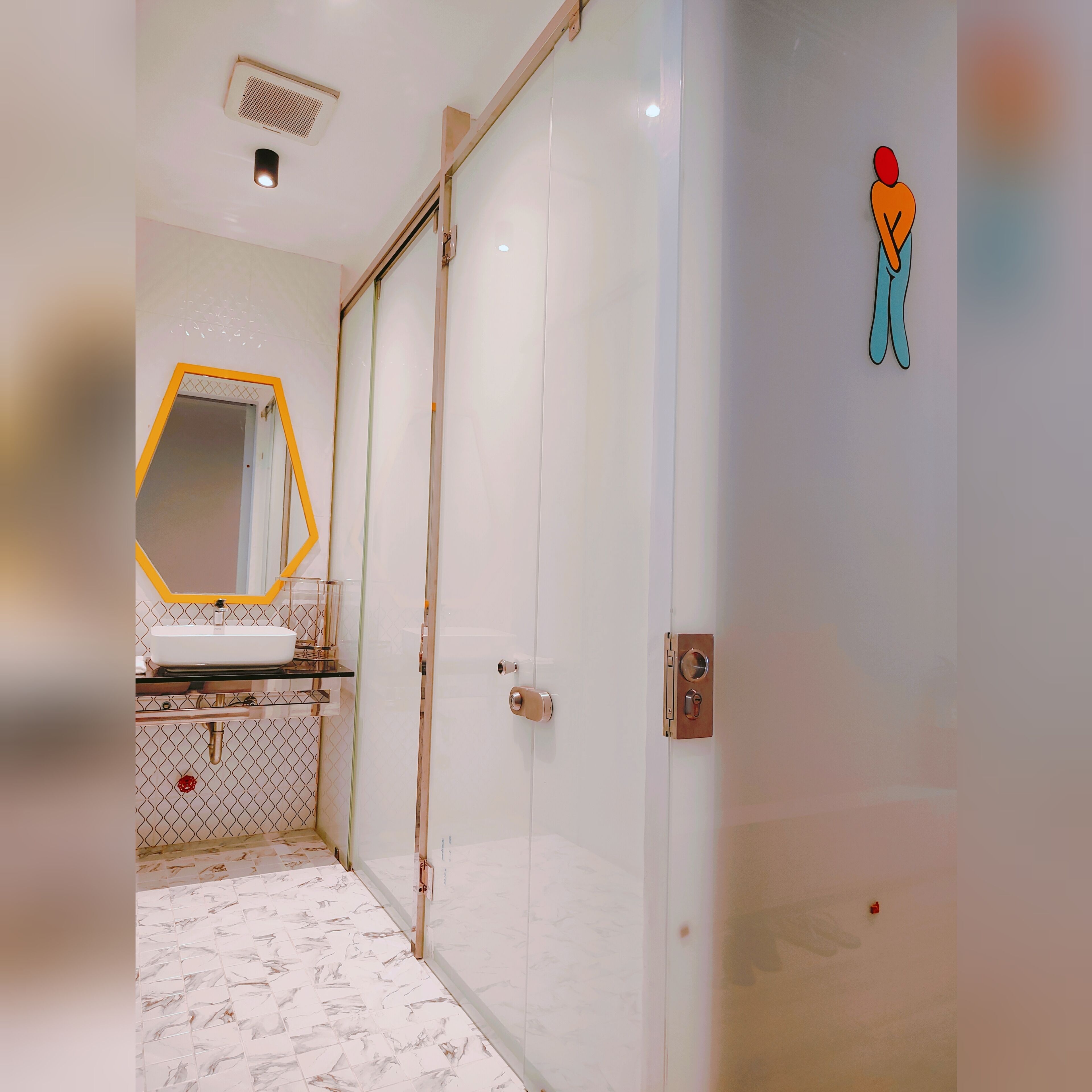 A bathroom with a white sink, a mirror with a yellow frame, a toilet, and a shower area.