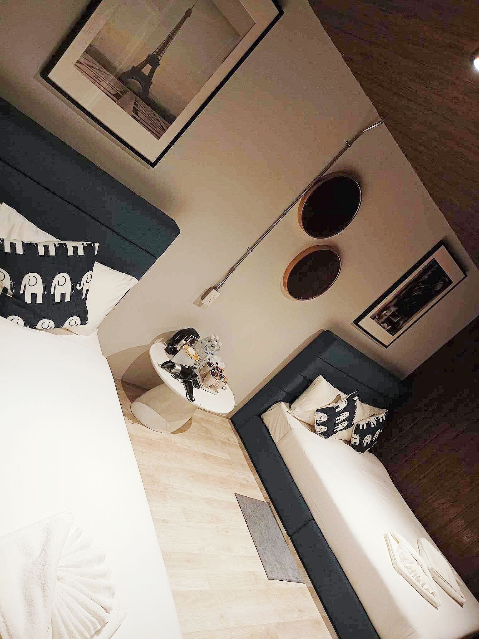 A modern hotel room with a bed, a small round table, and a sofa. There is a framed picture of the Eiffel Tower on the wall.